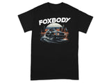 Black t-shirt with "FOXBODY" text and a drifting car graphic in a city at sunset.